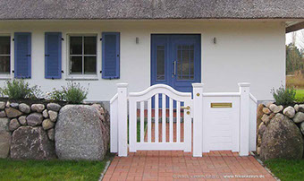 Wunderschönes Reetdachhaus mit einem typischem Friesenwall und einer weißen Gartentür mit Briefkasten.